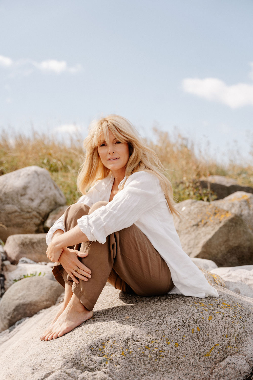     Linnea Leth seated on coastal rocks in white shirt and brown trousers